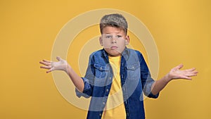 Puzzlement cute boy kid gesturing dont know not sure with spreading arms posing isolated on orange