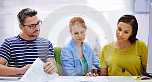 This is puzzling. three colleagues puzzled over some paperwork in an office setting.