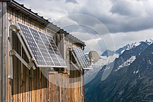 PV solar panels and satellite dish antenna at the wall of a wooden building with snowy mountains in the background