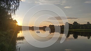 A PVC motorized inflatable boat floats on the river, while fishermen catch predatory fish by trolling. Illuminated by the summer s