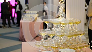 A pyramid of champagne glasses at a party against the backdrop of a hall with guests. champagne pyramid