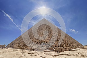 The Pyramid of Cheops illuminated by the sun in backlight, with people entering inside to visit it. The area with the great