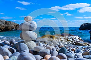 A pyramid of four pebbles is built on the beach against the background of blue sky and sea