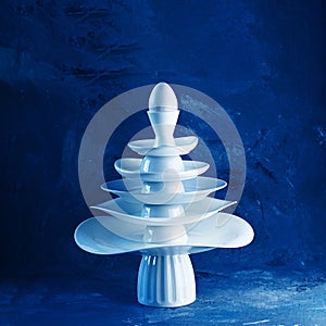 Pyramid made from white dishes, Christmas tree shape with egg on top on dark background. Creative concept dishware, kitchen,