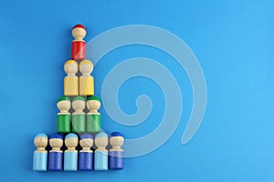 Pyramid of multicolored wooden toy people on blue background with copy space, concept of social rating