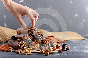 Pyramid pastilles dried fruits, nuts, honey with hand on grey background, Eastern sweetness concept, fruit roll-up