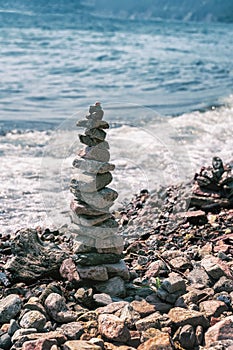 Pyramid of pebbles on the beach on a background of the sea wave. Stability, balance and harmony, vacation at sea