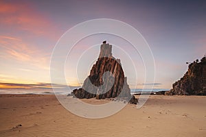 Pyramid sea stack on beach with beautiful sunrise sky with red clouds