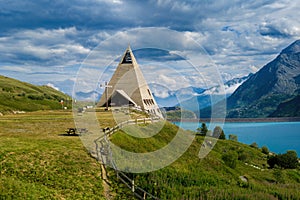 Pyramid shaped church, alpine lake of Mont-Cenis and mountains on background in France