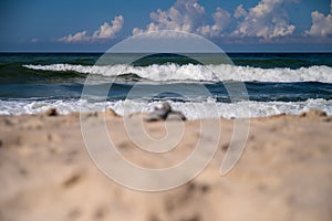 A pyramid of stones out of focus on the yellow sand on the seashore, against the background of white waves of the surf.