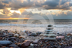 Pyramid of stones from pebble for meditation, on a background a seashore at sunset a sun. Marine background