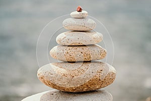 Pyramid stones on seashore with warm sunset on sea background for perfect holiday. Pebble beach and calm sea create a