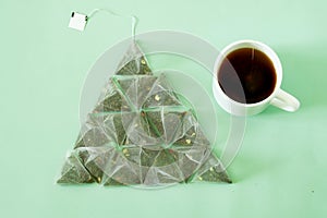 Pyramid tea bags with black and green tea, with pieces of fruit, and a white mug on a green background. Pyramid shape