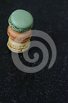 A pyramid of three colorful macaroons is on a black background. Three tasty cookies