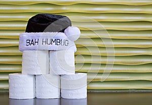 A pyramid of toilet paper with a Bah Humbug hat against a gold background