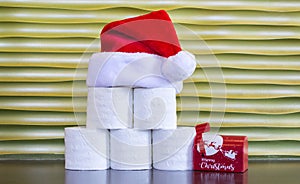 A pyramid of toilet paper with a Santa Claus hat and tiny mailbox  against a gold background