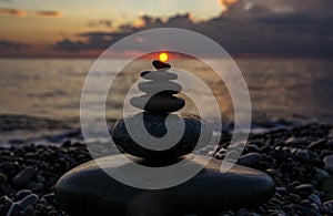 Pyramid or tower of pebble stones with sun against the background of the sea and the sunset sky. Zen stones, meditation concept