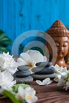 Pyramids of gray zen stones with white flowers, green leaves on wooden background. Concept of harmony, balance and meditation,