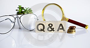 Q A concept on the wooden cubes and flower ,glasses ,coins and magnifier on white background