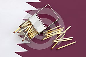 Qatar flag is shown on an open matchbox, from which several matches fall and lies on a large flag