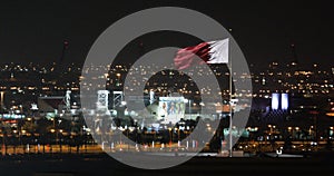 The Qatari flag at night above the city Doha