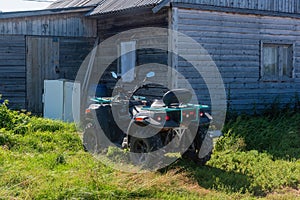 quad bike ATV is standing in the grass next to an abandoned wooden house. the concept of travel and tourism.
