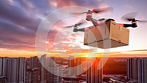 Quadcopter drone with cardboard box flying over the city at sunset