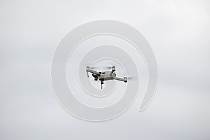 The quadcopter flies in height against the background of a gray sky.