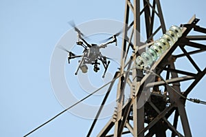 Quadcopter flying in a sky, electric pylon, cables and insulators on background