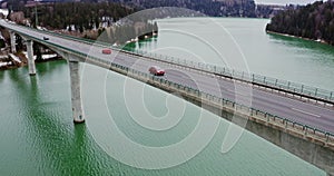 Quadcopter video of a bridge across a river to hills covered in snowy forest.