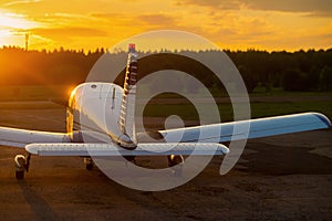 Quadruple aircraft parked at a private airfield. Rear view of a plane with a propeller on a sunset background.