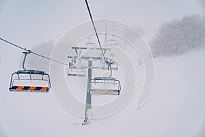 Quadruple chairlift rises above snowy forest to misty mountain