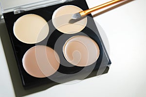 Quadruple skin tone eye concealer and contour palette with a beauty brush on a white background