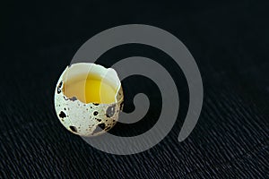 Quail egg on a black textured background. Raw broken egg with the yolk. Easter card.