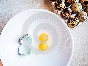 Quail egg with double yolk broken on a white plate.