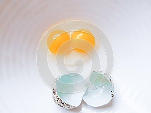 Quail egg with double yolk broken on a white plate.