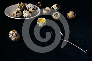 Quail eggs on a black textured background. Raw broken egg with the yolk. Easter card. Side view.