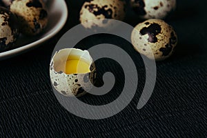 Quail eggs on a black textured background. Raw broken egg with the yolk. Easter card. Side view.