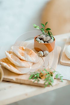 Quail eggs in a bowl with bread and herbs as an Easter decoration on a wooden table in a bright room