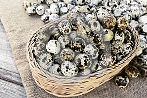 Quail eggs a lot of in basket and heap shell quail eggs on sackcloth of the wooden background.