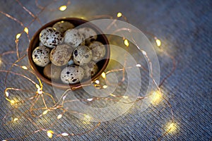 Quail eggs in a wooden plate on a blue background with golden lights.