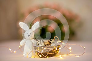 Quail eggs in a wooden plate and an easter toy bunny on a pink background.