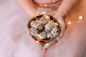Quail eggs in a wooden plate in the hands of a girl on a pink background.