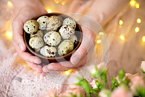 Quail eggs in a wooden plate in the hands of a girl on a pink background.