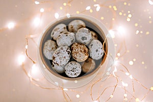 Quail eggs in a wooden plate on a pink background with golden lights.
