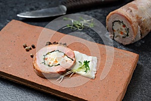 Quail galantine, de-boned stuffed meat for a festive dinner served on a rustic brick plate on a dark table, copy space photo