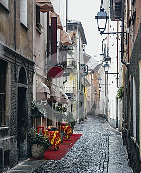 Quaint cobblestone alleyway in Aosta Italy with inviting red carpet entrance to Italian restaurant on left