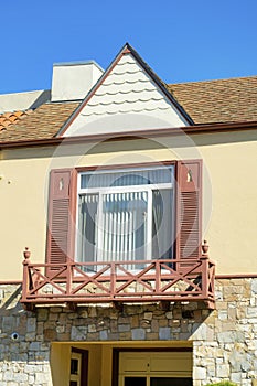 Quaint house facade with brown roof and white and beige stucco paint with red shudders and small balcony with blue sky photo