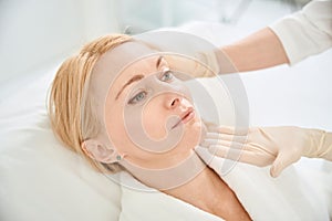 Qualified beautician looking at adult woman face, checking state of skin