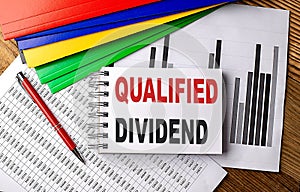 QUALIFIED DIVIDEND text on a notebook with pen, folder on a chart background